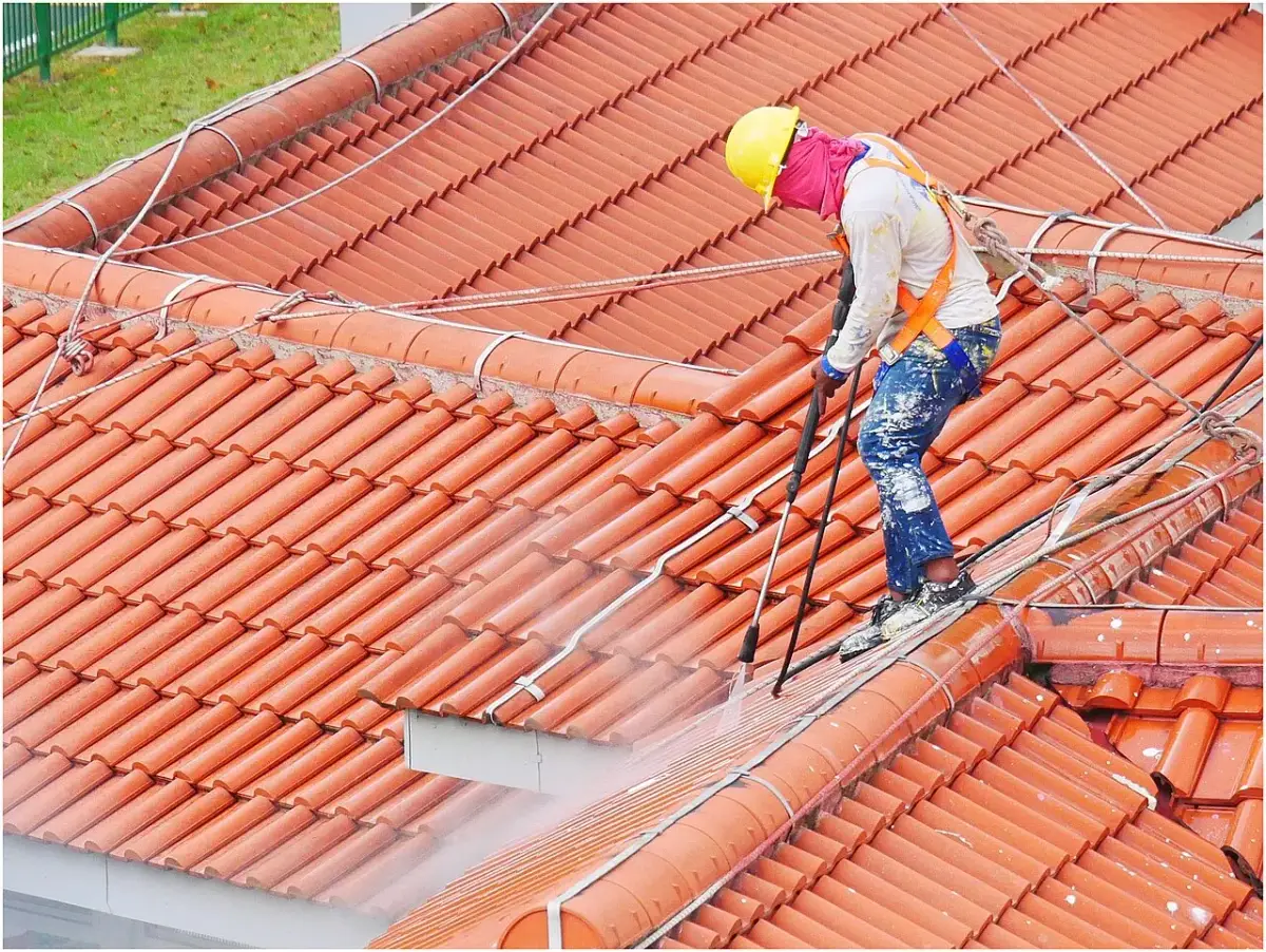Worker using a pressure washer to clean an exterior roof surface